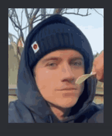 a man wearing a black beanie and a hoodie is eating a potato chip .