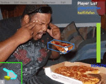 a man is sitting at a table with a box of pizza and a player list displayed on the screen behind him