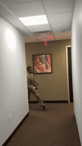 a man is walking down a hallway with a red exit sign above him
