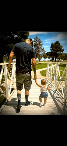 a man is holding a baby 's hand while they walk across a bridge .