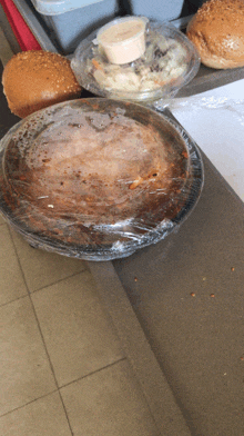 a plastic container of food sits on a counter next to a hamburger