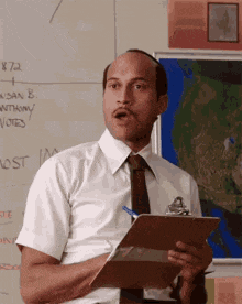 a man in a white shirt and tie is holding a clipboard in front of a board with the number 872 written on it