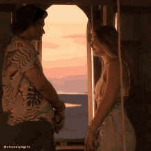 a man and a woman are looking at each other in front of a window overlooking the ocean