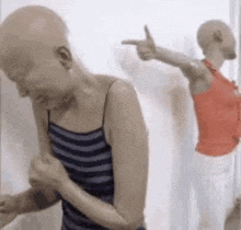 a bald woman in a striped shirt is pointing at another bald woman in a red tank top .