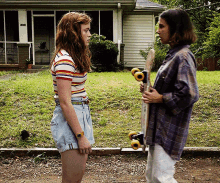 a woman holding a skateboard stands next to another woman in front of a house that has the number 1018 on it