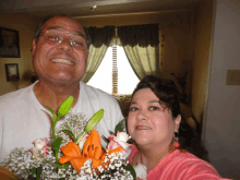 a man and a woman are posing for a picture with flowers in front of a window