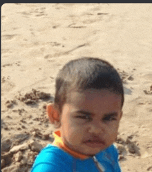 a young boy in a blue shirt is sitting on a beach looking at the camera .