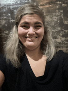 a woman with blonde hair wearing a black shirt smiles for the camera