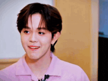 a young man wearing a pink shirt and earrings is smiling and looking at the camera .