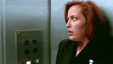 a woman with red hair is standing in an elevator looking at the buttons .