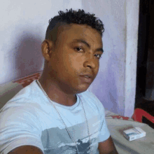 a man in a blue shirt is sitting on a bed with a pack of cigarettes in his hand .