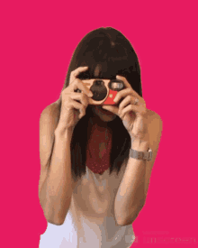 a woman is holding a camera in front of her face with a pink background