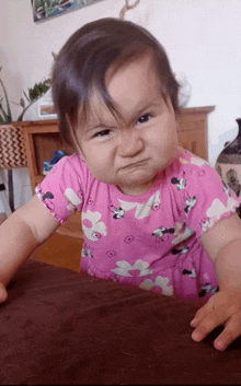 a baby girl wearing a pink minnie mouse dress making a funny face