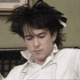 a man with black hair is wearing a white shirt and suspenders and looking down .