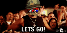 a man wearing a helmet and sunglasses stands in front of a crowd and says lets go