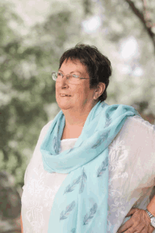 an older woman wearing glasses and a blue scarf smiles