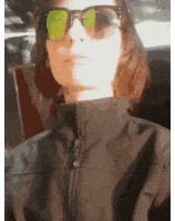 a woman wearing sunglasses and a black jacket has a green sticker on her face