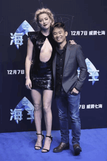 a woman in a black dress stands next to a man on a blue carpet