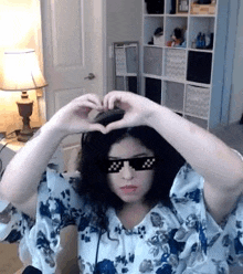 a woman wearing sunglasses and making a heart with her hands .