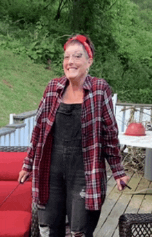 a woman wearing a plaid shirt and overalls is standing on a deck .