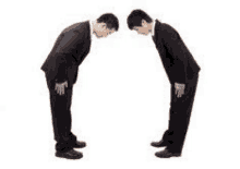 two businessmen in suits are bowing to each other .