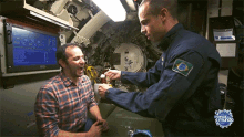 a man in a plaid shirt is talking to a man in a military uniform with a badge that says brasil