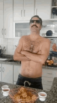 a shirtless man with a mustache and sunglasses is standing in a kitchen with his arms crossed