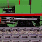 a green train is on the tracks with a red stripe on the side