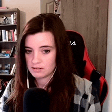 a woman wearing headphones and a plaid shirt is sitting in front of a microphone in front of a book shelf .