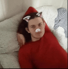 a man in a red sweater is laying on a bed with cat ears on his head .