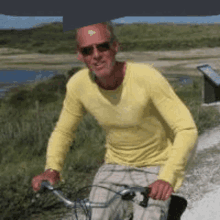 a man wearing sunglasses and a yellow shirt is riding a bicycle on a dirt road .