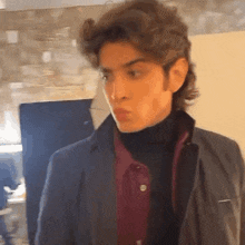 a young man wearing a turtleneck and a black jacket looks at the camera