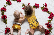 two babies are laying on a bed with flowers around them and one has a b on his diaper