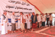 a group of men are shaking hands in front of a sign that says ' من أجل حضرموت '