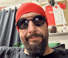 a man with a beard wearing sunglasses and a red beanie with etoro on it