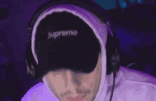 a man wearing headphones and a supreme hat is sitting in front of a computer .