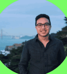 a man wearing glasses stands in front of a bridge overlooking the ocean