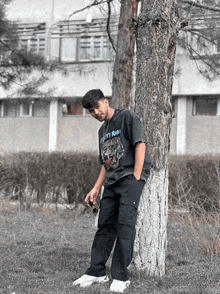 a young man leaning against a tree wearing a t-shirt that says dirty ron