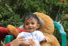 a baby is sitting on a green chair with a teddy bear behind him