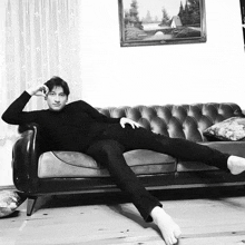 a black and white photo of a man laying on a couch with his legs crossed