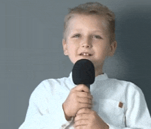 a young boy in a white shirt is holding a microphone in his hand .