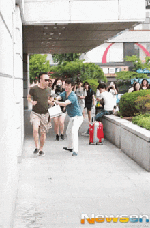 a group of people are running down a sidewalk with a red suitcase in front of a building that says newson