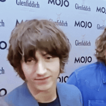 a young man stands in front of a wall that says mojo