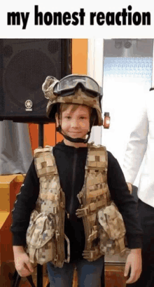 a young boy dressed as a soldier with a helmet and goggles is standing in front of a speaker .