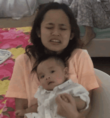 a woman is holding a baby in her arms and the baby is looking at the camera