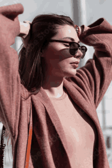 a woman wearing sunglasses and a sweater holds her hair