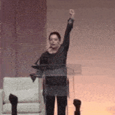 a woman is standing at a podium with her fist in the air while giving a speech .