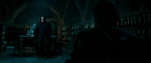 a man in a black coat stands in a dark room with bottles on shelves and a man in a black jacket