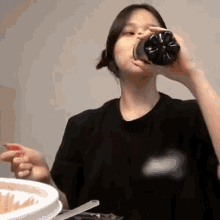 a woman is drinking soda from a plastic bottle while sitting at a table with a plate of food .