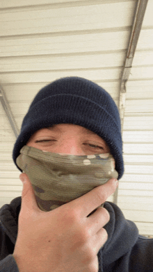 a man wearing a blue beanie and a camouflage mask covering his face